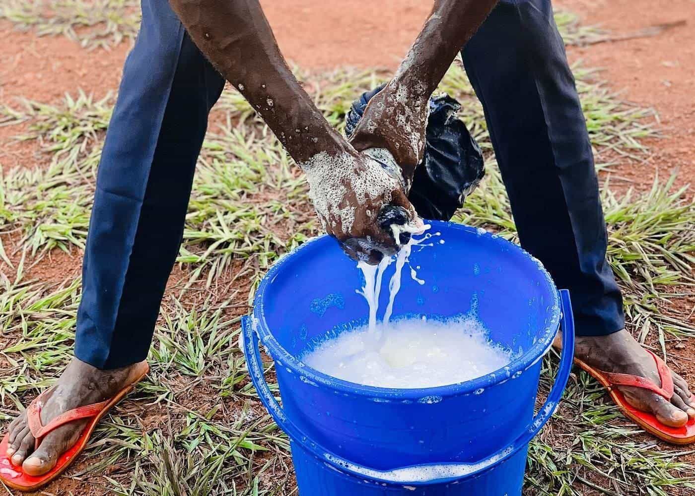 A person hand washing clothes in a blue bucket
